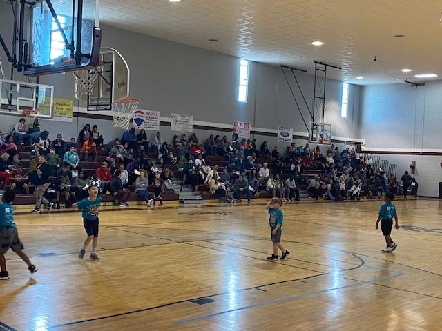 Youth basketball game with teal uniforms and packed bleachers